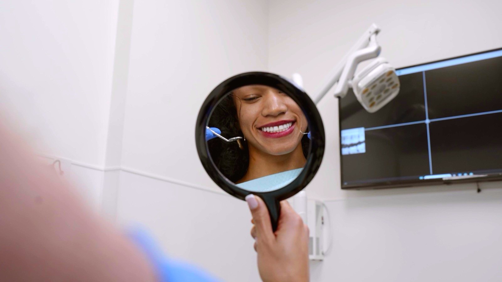 A patient’s smile reflected in a hand mirror