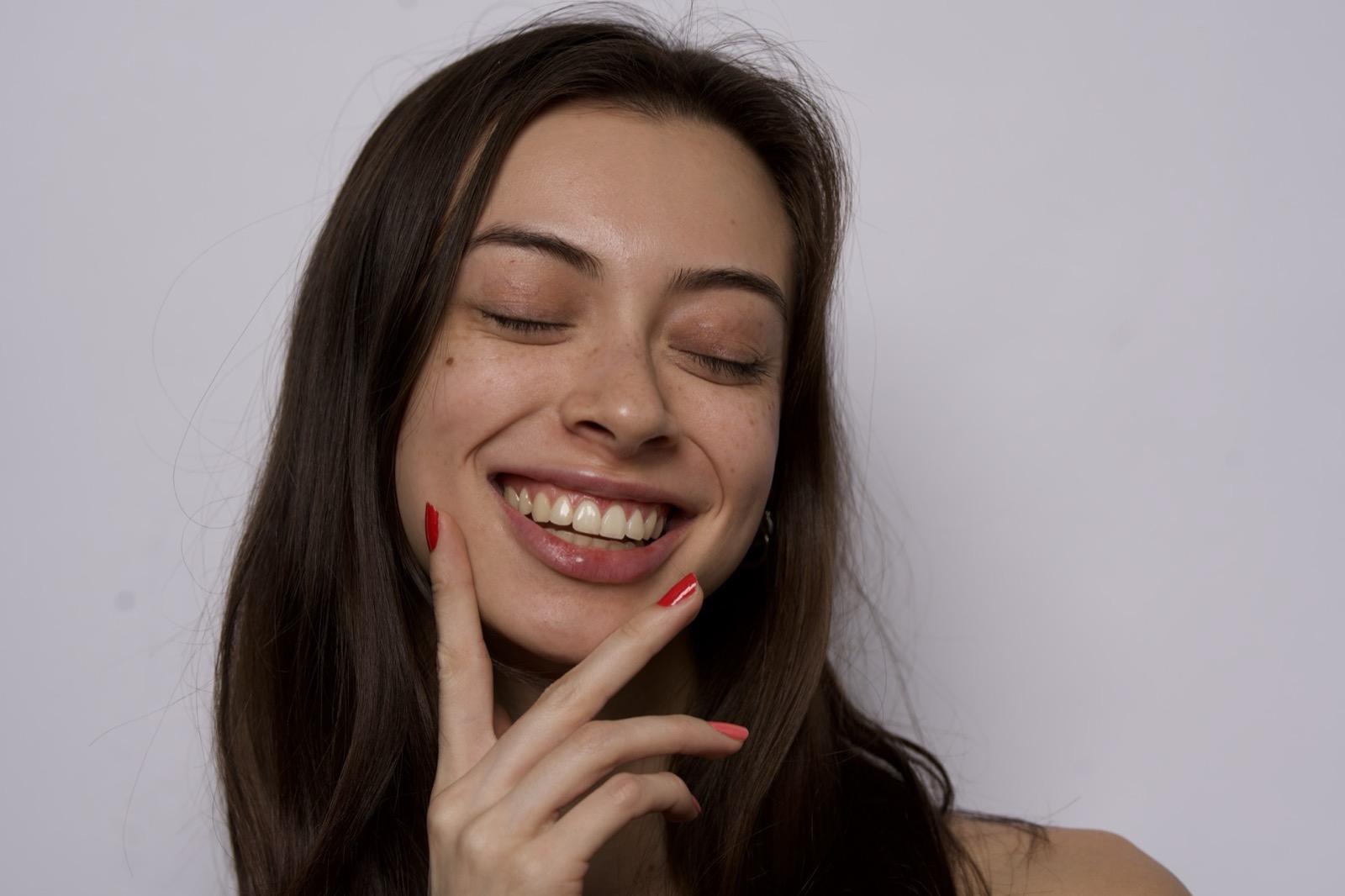 A woman smiling, eyes closed, her hand at her cheek