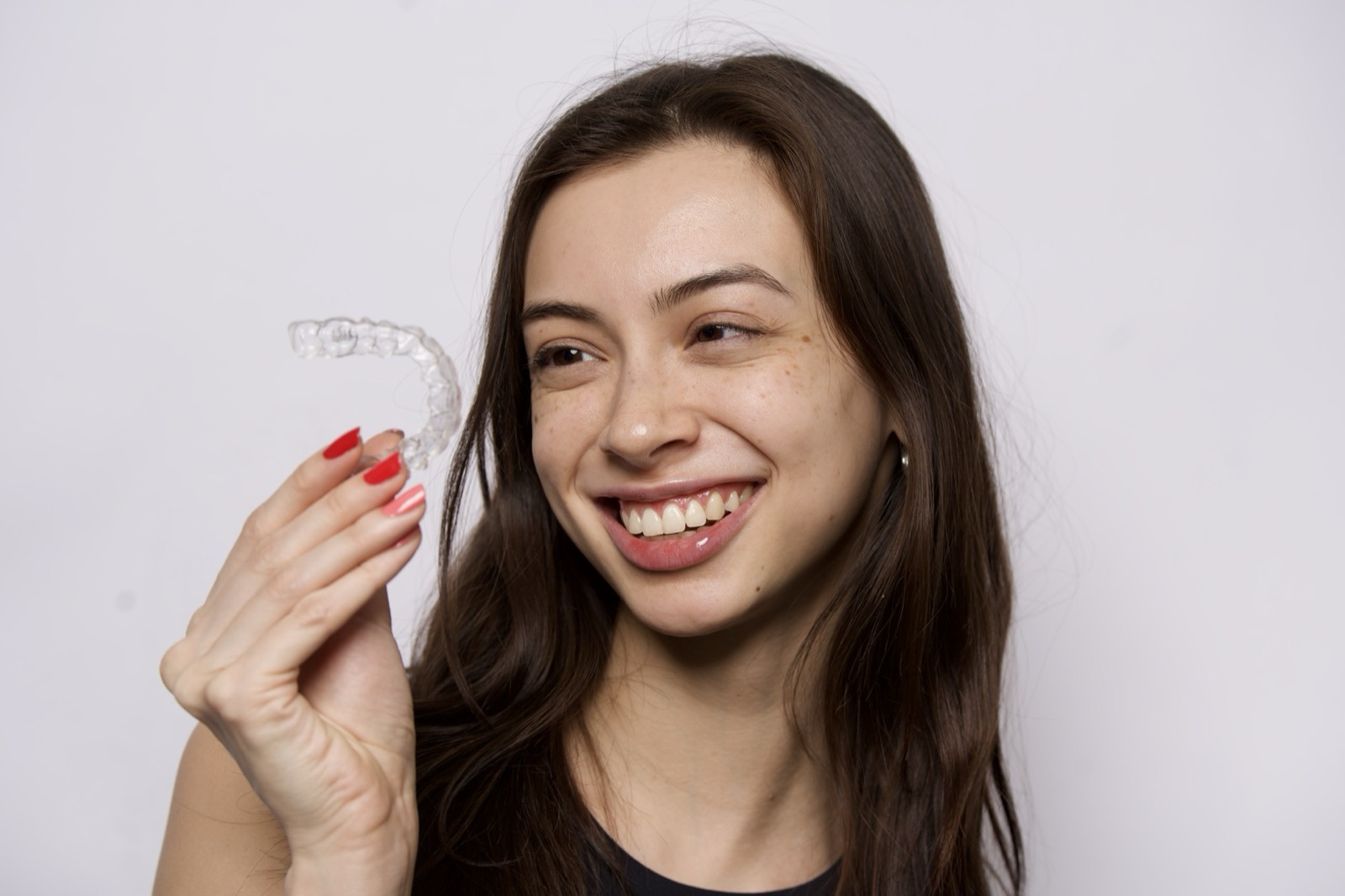 A woman holding a clear aligner, smiling to the side